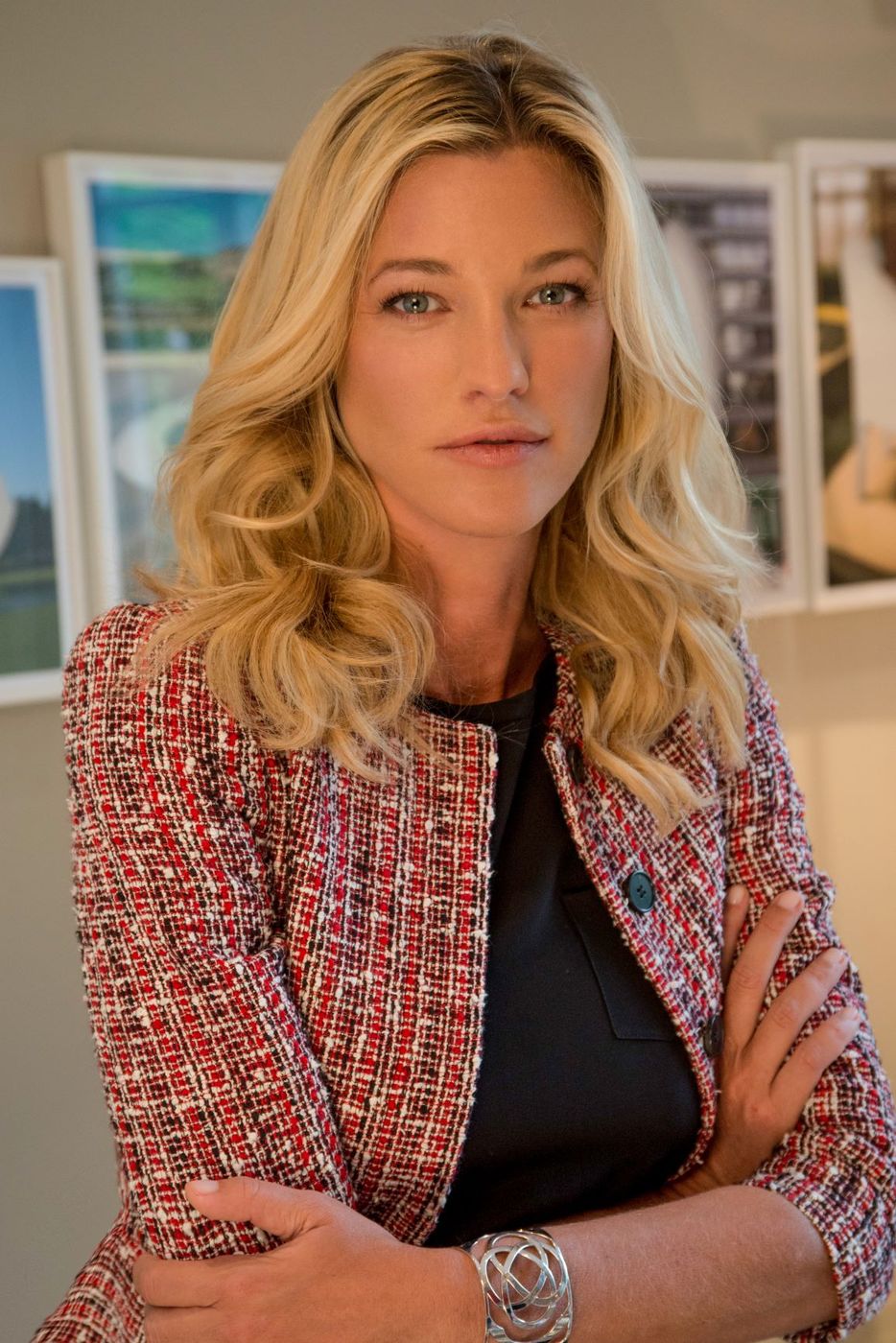 Nicole Junkerman steht mit verschränkten Armen in einem hellen Raum, hinter ihr gerahmte Bilder an der Wand