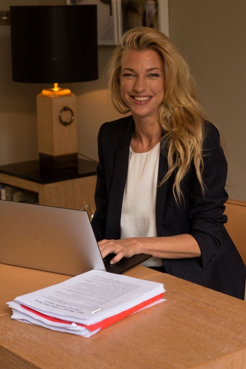 Nicole Junkerman lächelt an ihrem Schreibtisch und arbeitet an einem Laptop mit Notizen und Unterlagen.