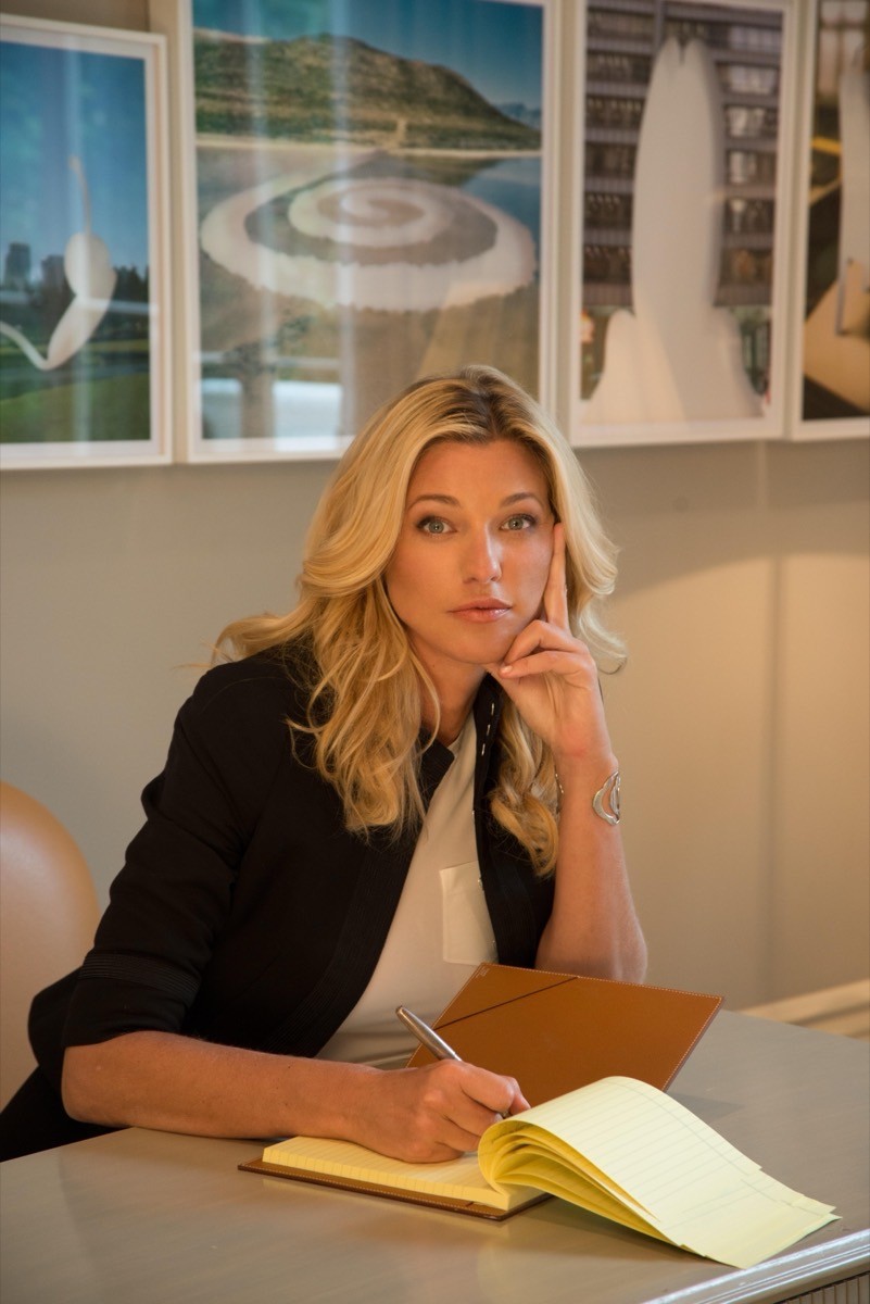 Nicole Junkerman macht sich nachdenklich Notizen in ein Notizbuch, im Hintergrund gerahmte Kunstdrucke.