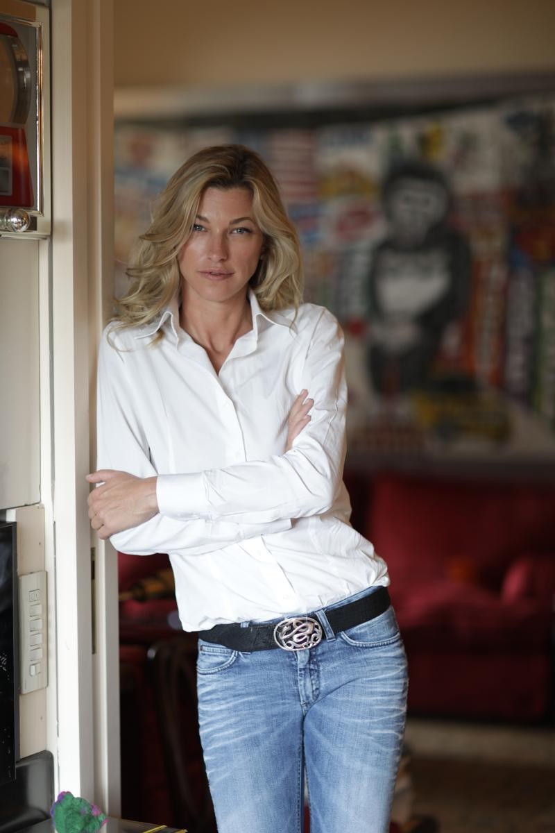 Nicole Junkerman lehnt entspannt in einem Türrahmen ihres Zuhauses, im Hintergrund moderne Kunst und ein rotes Sofa.
